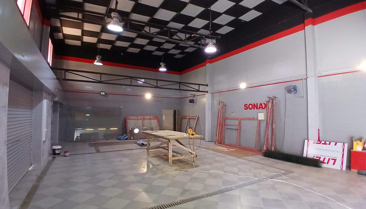 Interior of a semi-fitted industrial garage with a checkered ceiling, scattered tools, and a central work table.