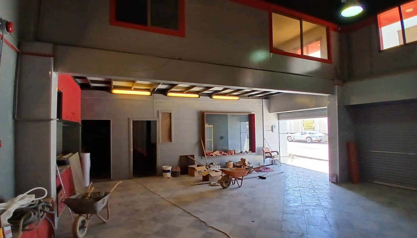 A spacious semi-fitted shop with construction tools and materials scattered around, featuring overhead windows and open roller doors.