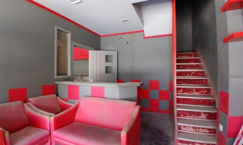 Interior of a semi-fitted shop with a red and gray color scheme, featuring two red sofas, a staircase, and an open cabinet.