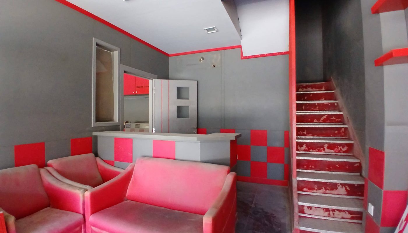 Interior of a semi-fitted shop with a red and gray color scheme, featuring two red sofas, a staircase, and an open cabinet.