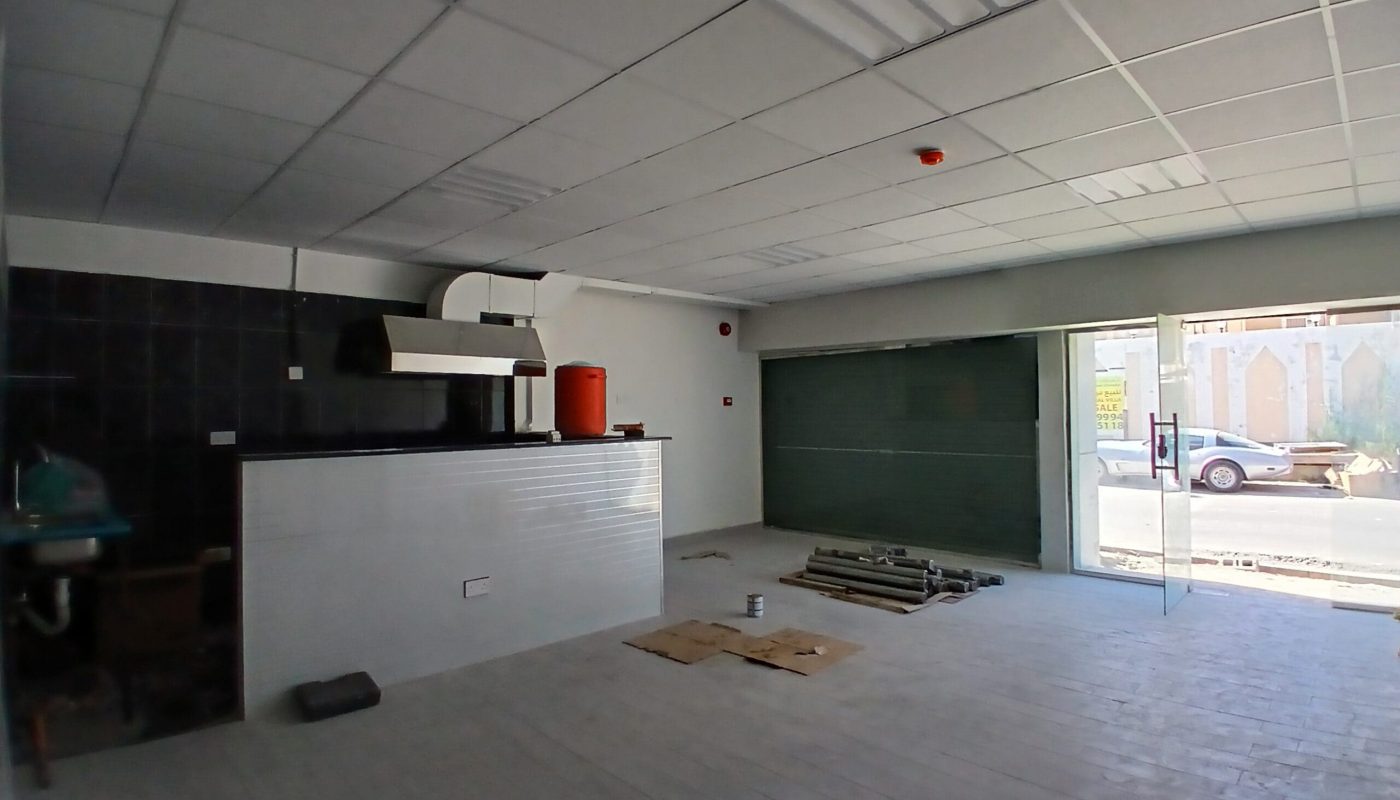 Empty commercial space with a counter, tiled wall, and large front window, overlooking a street with an auto draft.