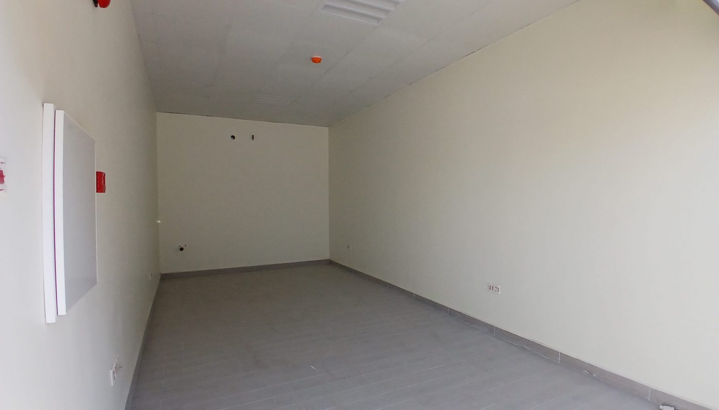 متجر بيع بالتجزئة شبه مجهز بجدران رمادية فاتحة وأرضية رمادية داكنة وسقف أبيض مع مجاري هواء مرئية ومعدات السلامة من الحرائق.