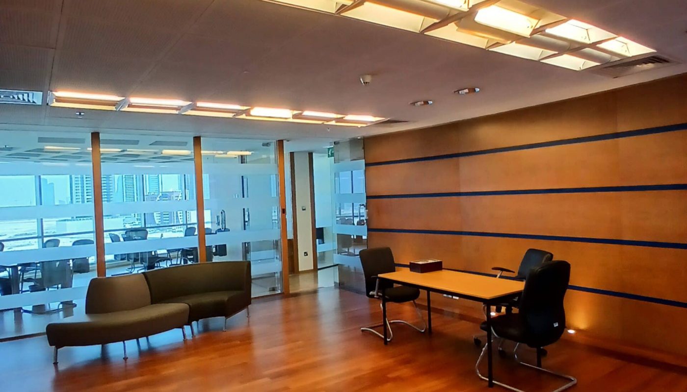 Modern office meeting room with wooden flooring, a long Auto Draft table with chairs, and a sofa, brightly lit by overhead lights.
