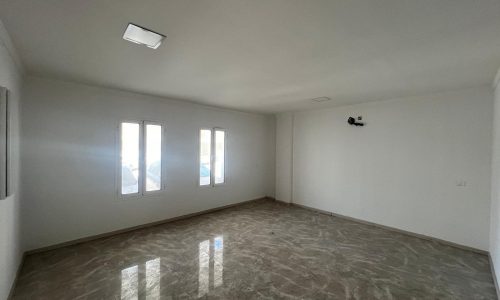 An empty flat for rent with white walls, two windows, and glossy marble flooring in Al Hidd.