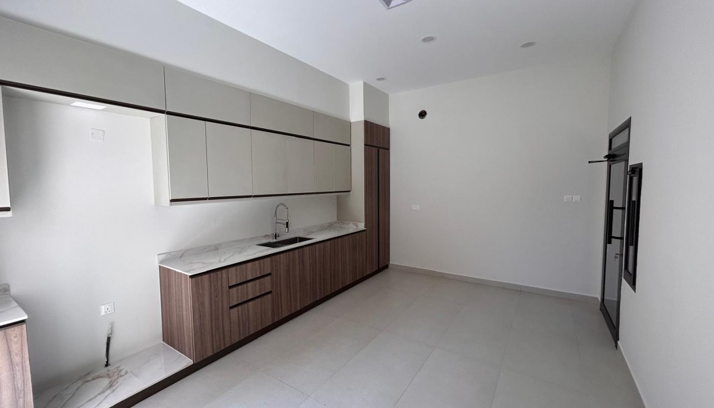 Modern, unfurnished kitchen with wood and white cabinets, marble countertops, a sink, and large floor tiles. The space appears clean and minimalistic with neutral colors.