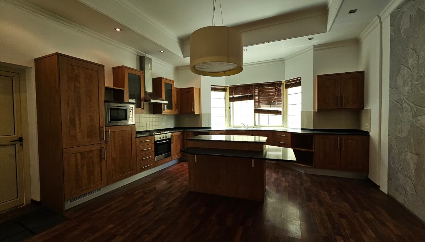 Modern kitchen with wooden cabinets, black countertops, an island in the center, built-in appliances, and large windows letting in natural light.
