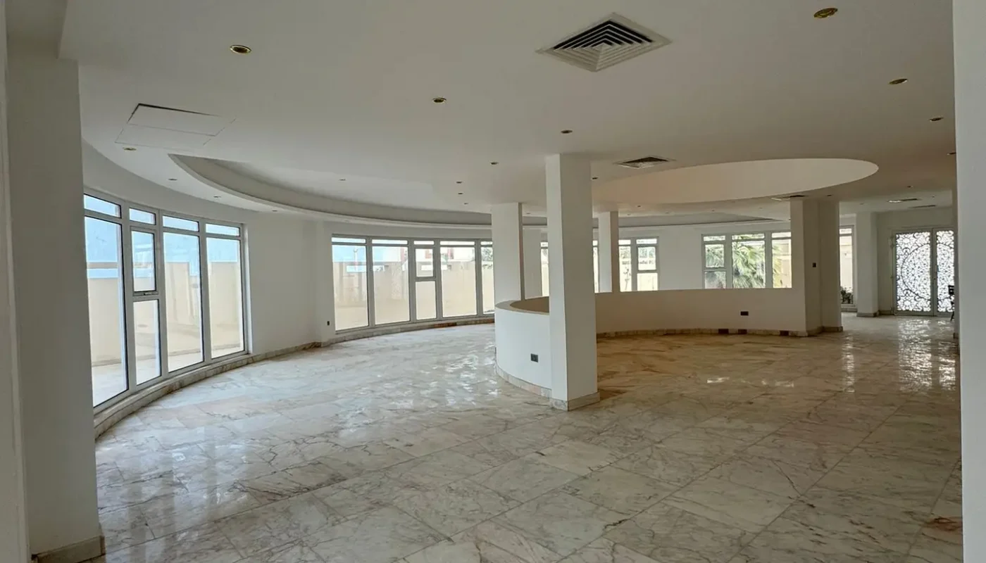 Spacious, empty room with marble floors, large windows, and glass doors leading to an outdoor area; white walls and ceiling with recessed lighting.