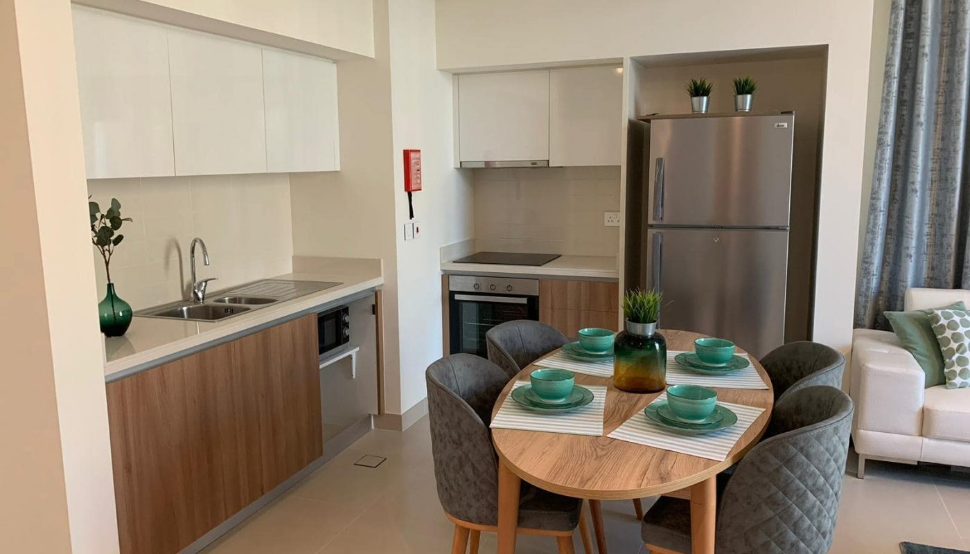 Modern kitchen and dining area with wood and white cabinets, stainless steel appliances, a round table set for four, and a small sofa in the corner.