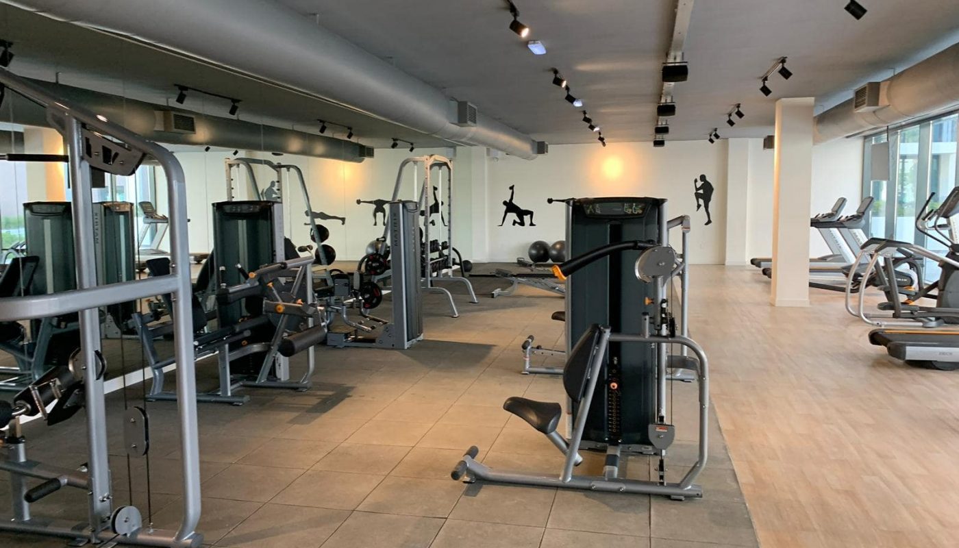 A modern gym with various exercise machines, weight equipment, and cardio machines, featuring a clean, spacious layout and wall art of athletic figures.