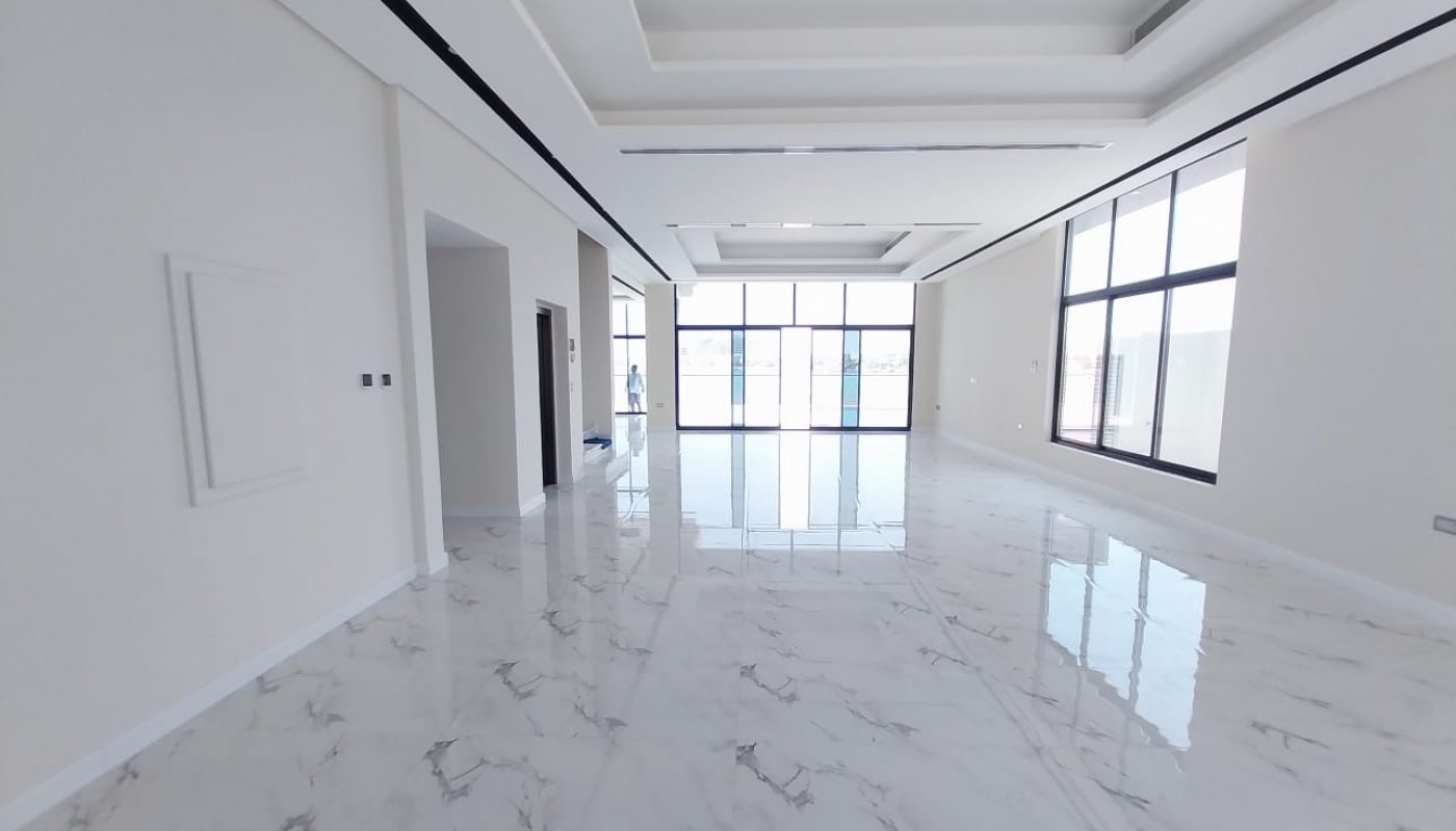 Spacious empty room with marble flooring, large windows, and high ceiling. White walls and ceiling with recessed lighting.