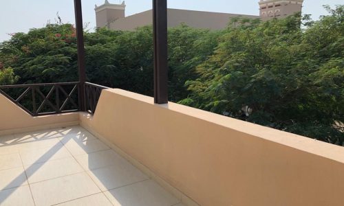 A balcony with a view of trees and buildings in Al Jasra, offering a luxury villa for rent.