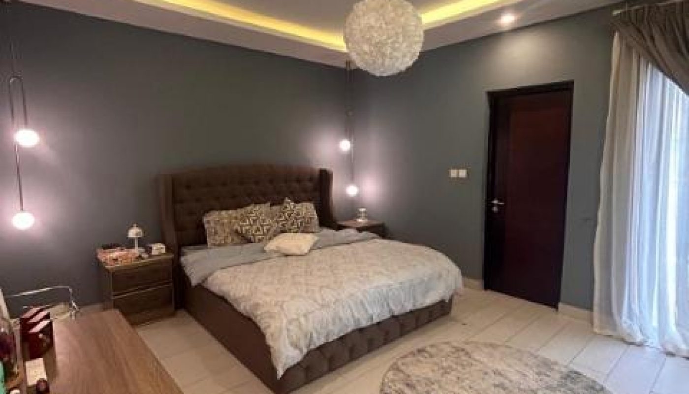 A bedroom with a king-size bed, modern lighting, and a dresser.