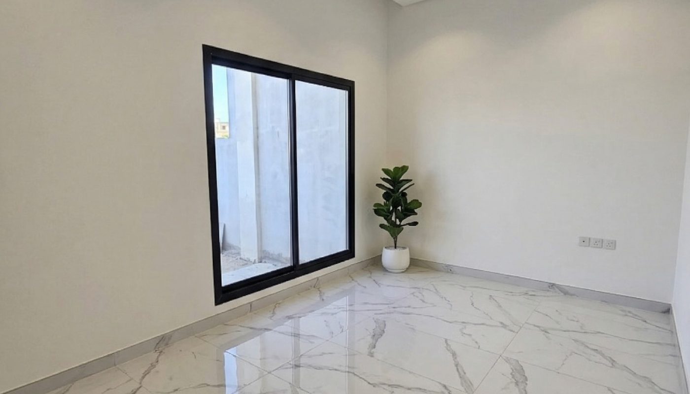A small, empty room with white walls, marble tile flooring, a large window, recessed ceiling lights, and a potted plant in the corner.