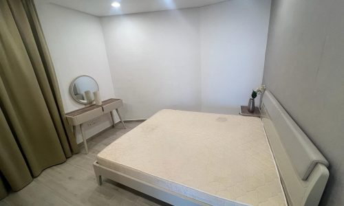 A small bedroom in an Amwaj flat with a bed and a mirror available for rent.