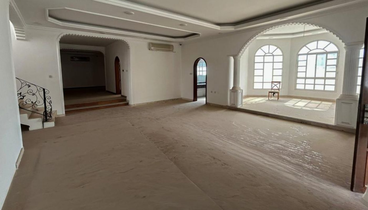 Empty, unfurnished room with large arched windows, white walls, and a covered floor. Stairs with a decorative railing lead up to an open doorway on the left.