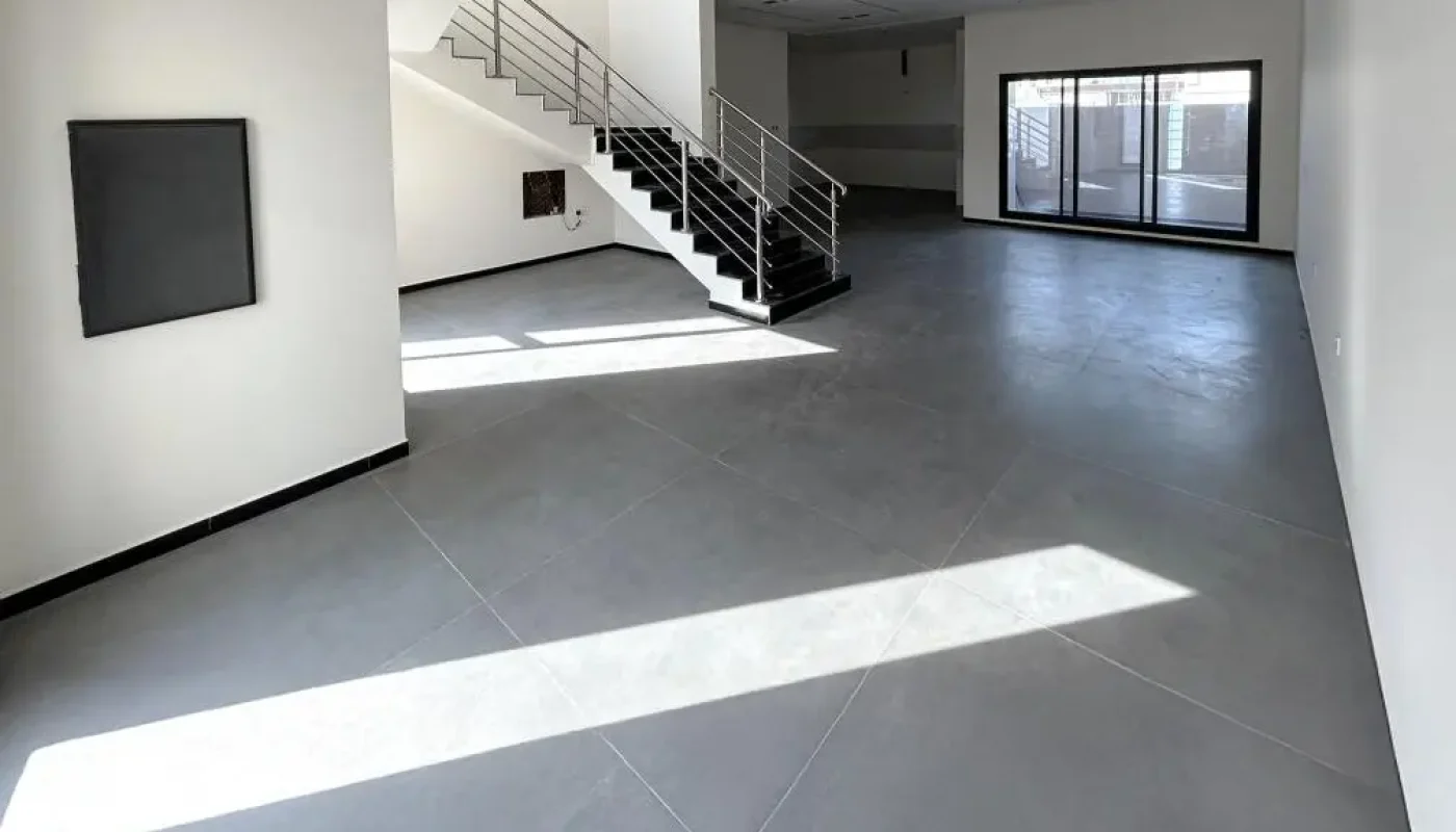 Spacious, empty modern interior with large gray tiled floor, black railing staircase, and floor-to-ceiling windows letting in natural light.