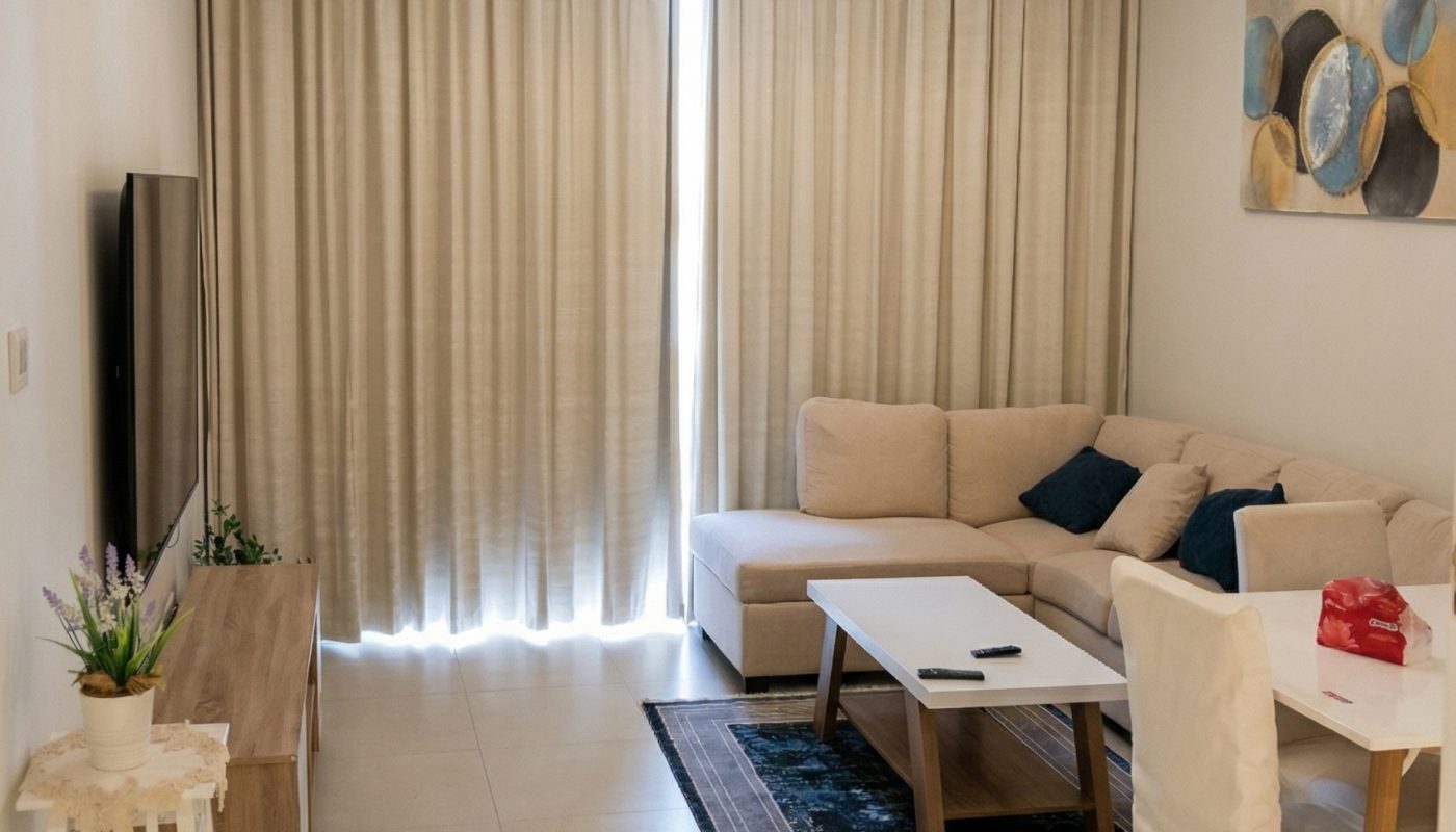 Modern living room with beige sofa, white table, TV on a wooden stand, abstract wall art, chandelier, and floor-to-ceiling curtains covering a window.
