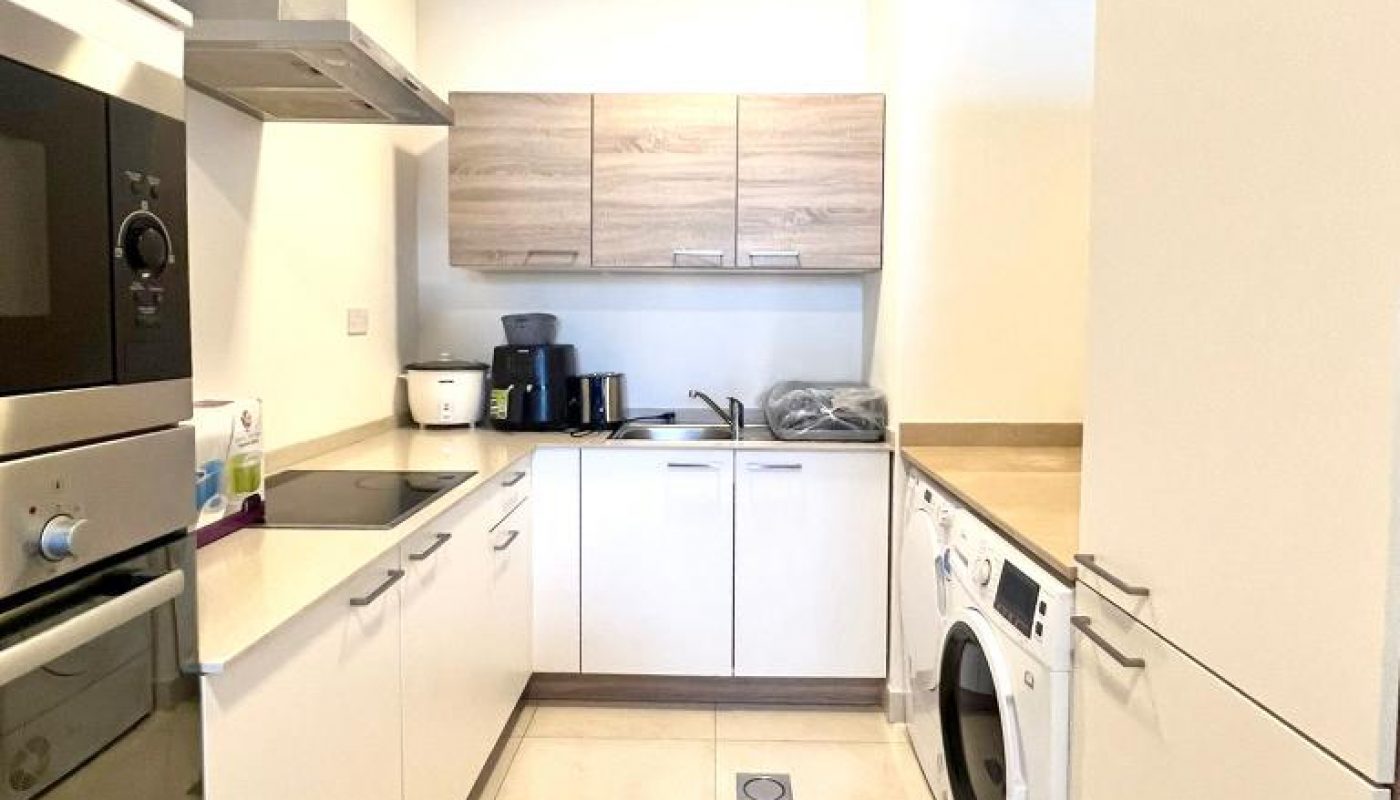 Modern kitchen with white cabinets, built-in oven and microwave, washing machine, countertop appliances, and light-colored tile floor.