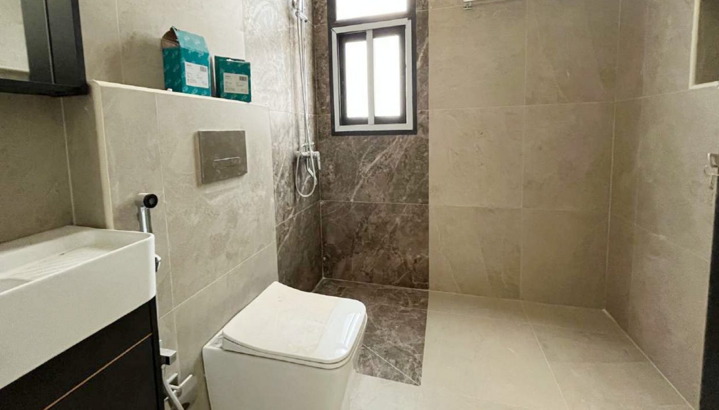Modern bathroom with beige and brown tiles, a wall-mounted toilet, a small sink, a window, a rain shower, a towel rack, and a floor mat.