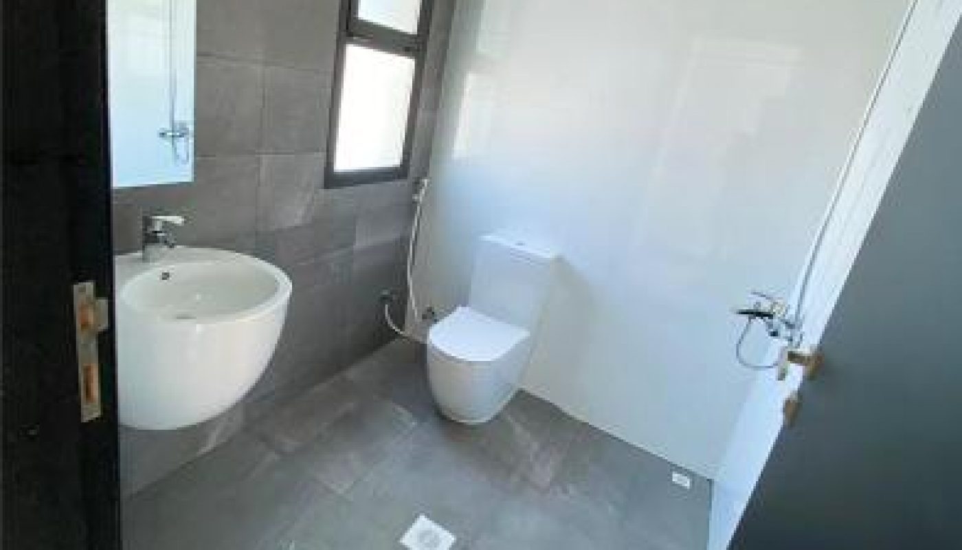 A modern bathroom with gray tile floors, a wall-mounted sink, a toilet, a window, and a mirror above the sink.