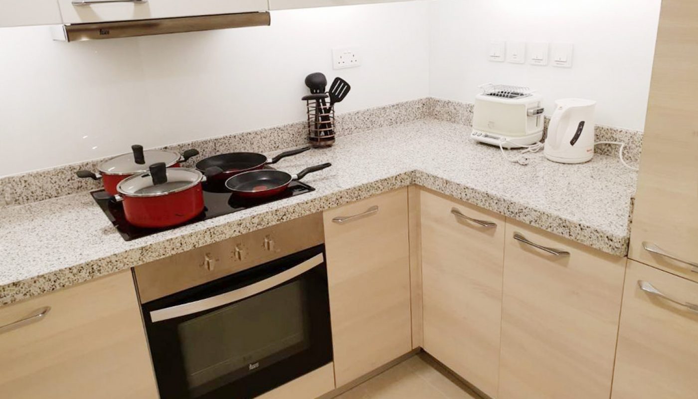 Modern kitchen with beige cabinets, granite countertop, electric stove with pots and pans, toaster, kettle, and spice rack.