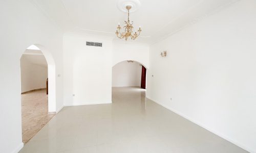 A spacious villa for rent in Mahooz, featuring an empty room with white walls and a chandelier.