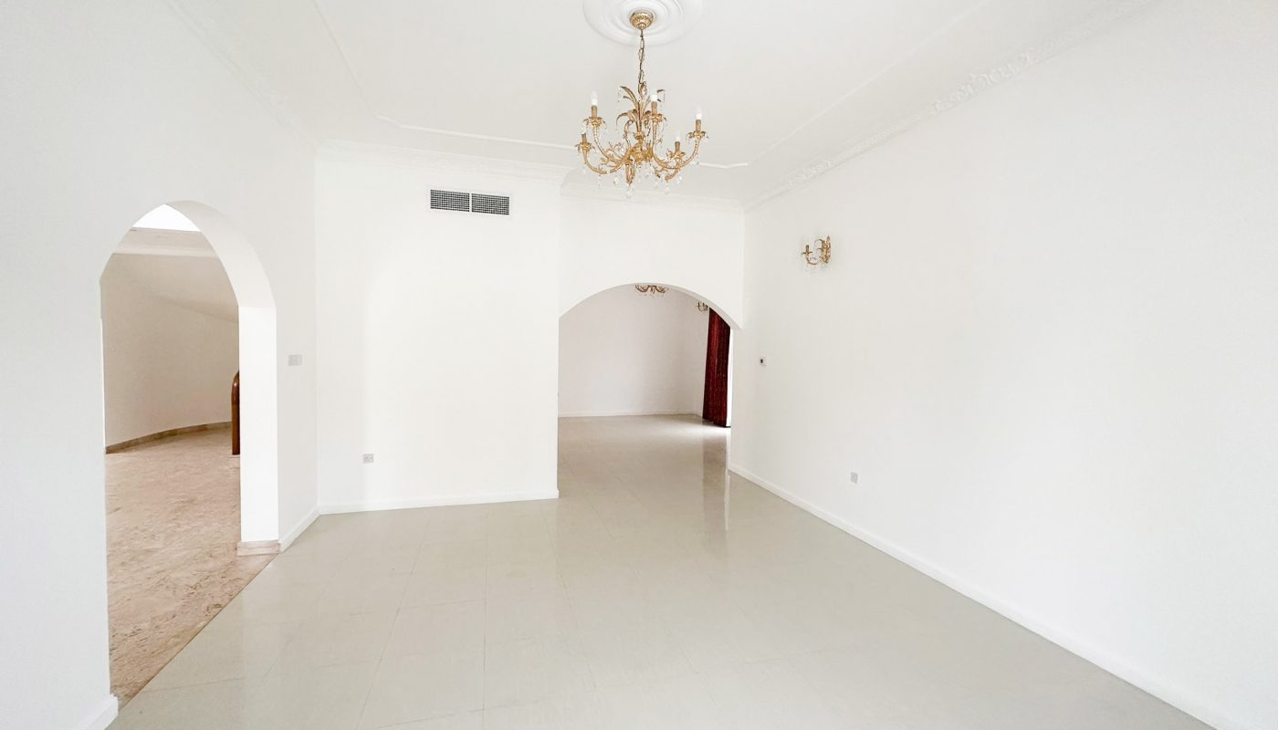 A spacious villa for rent in Mahooz, featuring an empty room with white walls and a chandelier.