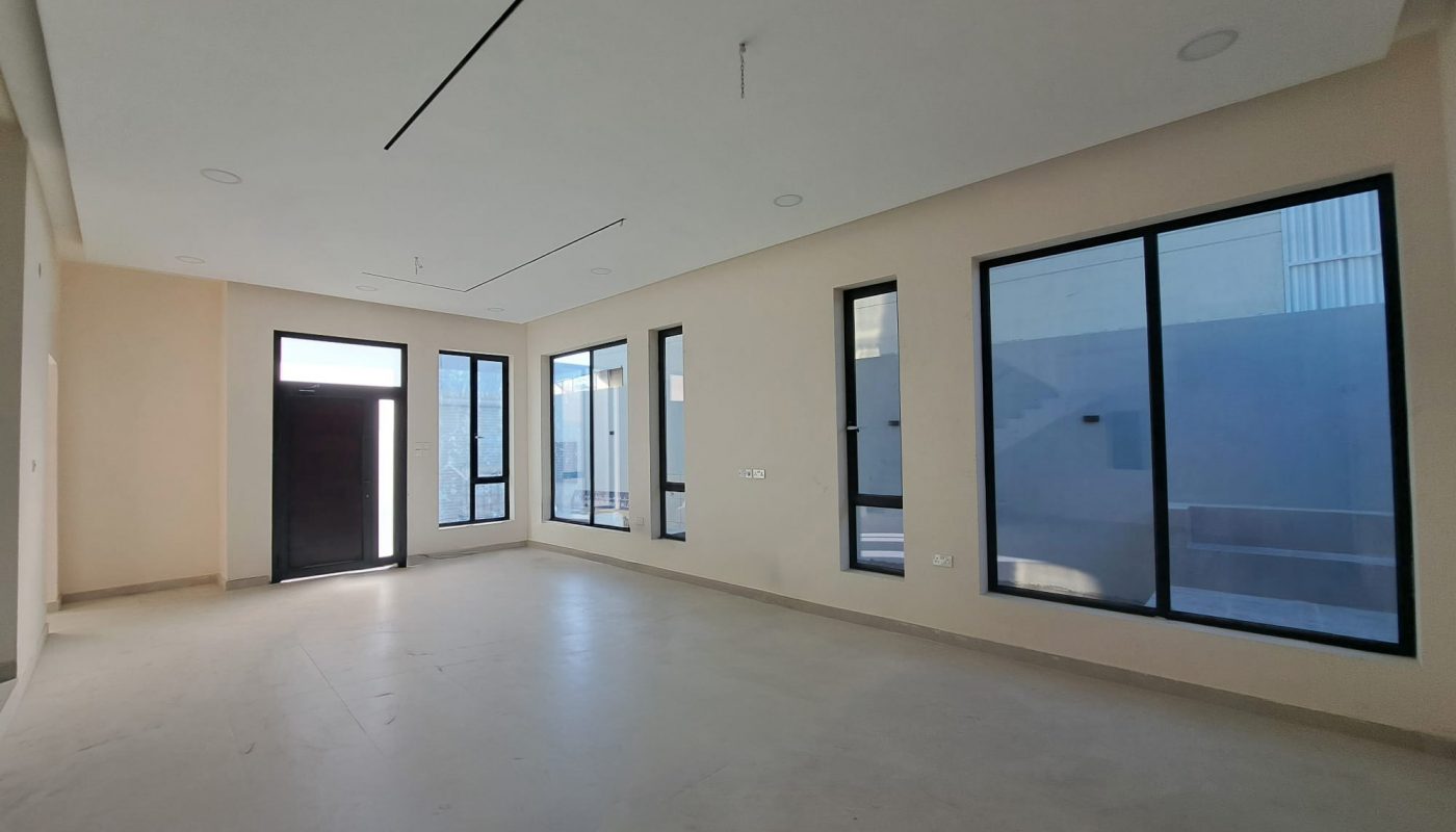 Empty modern room with large windows, white walls, beige floor, and a black door, letting in natural light from outside.