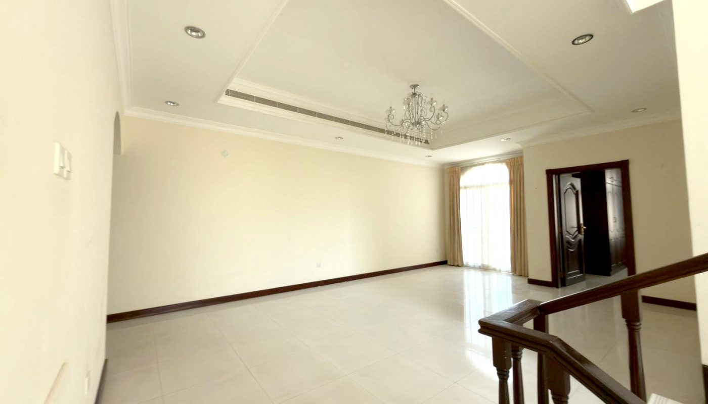 Spacious empty living room with white tiled floor, chandelier, large window with curtains, and staircase leading up.