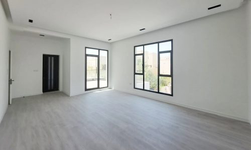 Empty modern villa for sale in a peaceful area with light gray floors, white walls, and large windows letting in natural light.