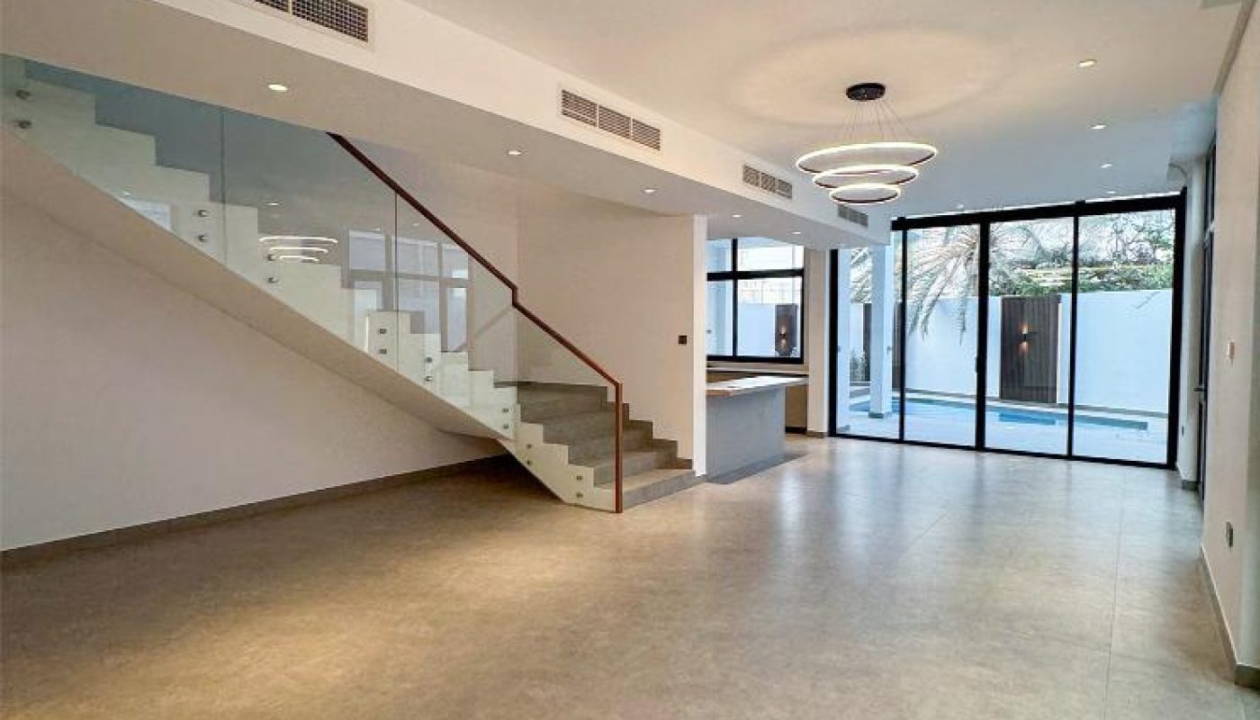 Spacious modern living area with large windows, a glass-railing staircase, recessed lighting, and an open connection to the kitchen.