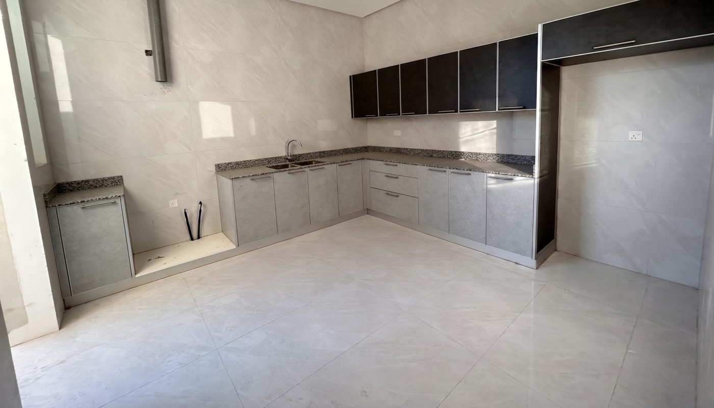 Modern, unfurnished kitchen with light gray tile floors, granite countertops, upper and lower cabinets, ceiling fan, and natural light from a window.