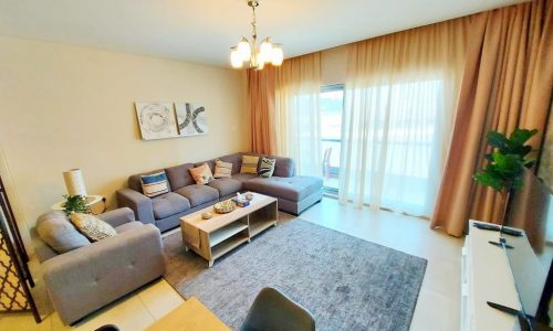 A modern living room with a couch and dining table, featuring a balcony.