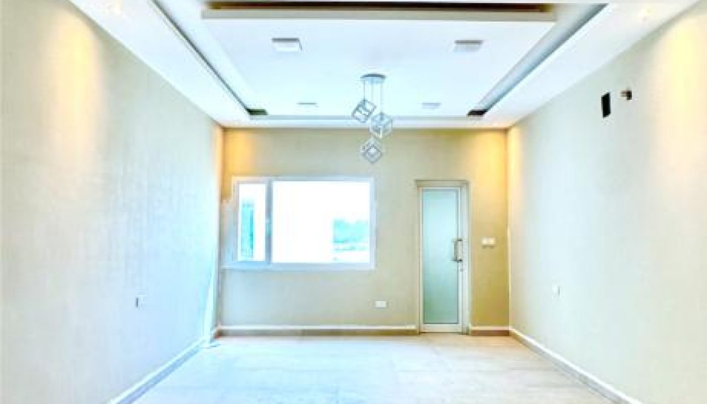 Empty, well-lit room with beige tiled floor, light-colored walls, a window, a glass door, and a modern ceiling light fixture.