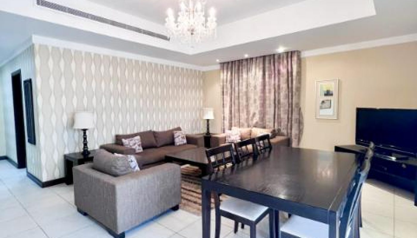 Modern living and dining area with a sectional sofa, dark dining table with chairs, chandelier, TV, and patterned wallpaper.