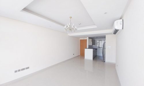 A Diyar Al Muharraq apartment available for rent with two bedrooms, featuring an empty room with white walls and a chandelier.