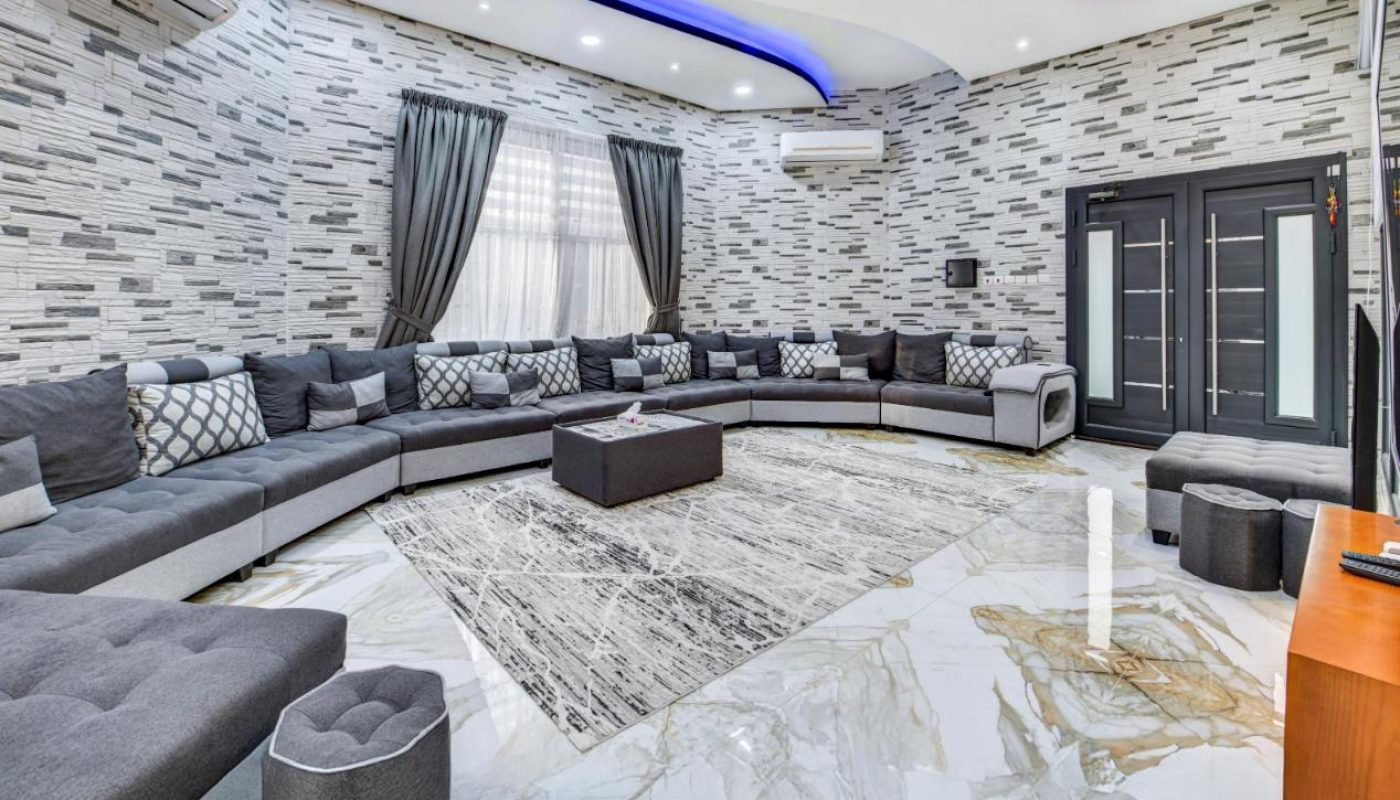 Modern living room with a large curved sectional sofa, marble floor, patterned walls, ceiling LED lights, and two black coffee tables.