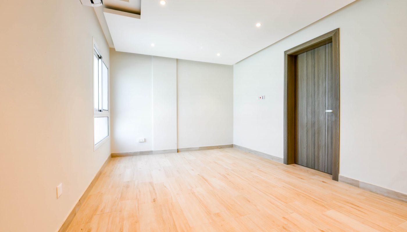 A spacious empty room in an apartment with wooden floors and a door available for rent.