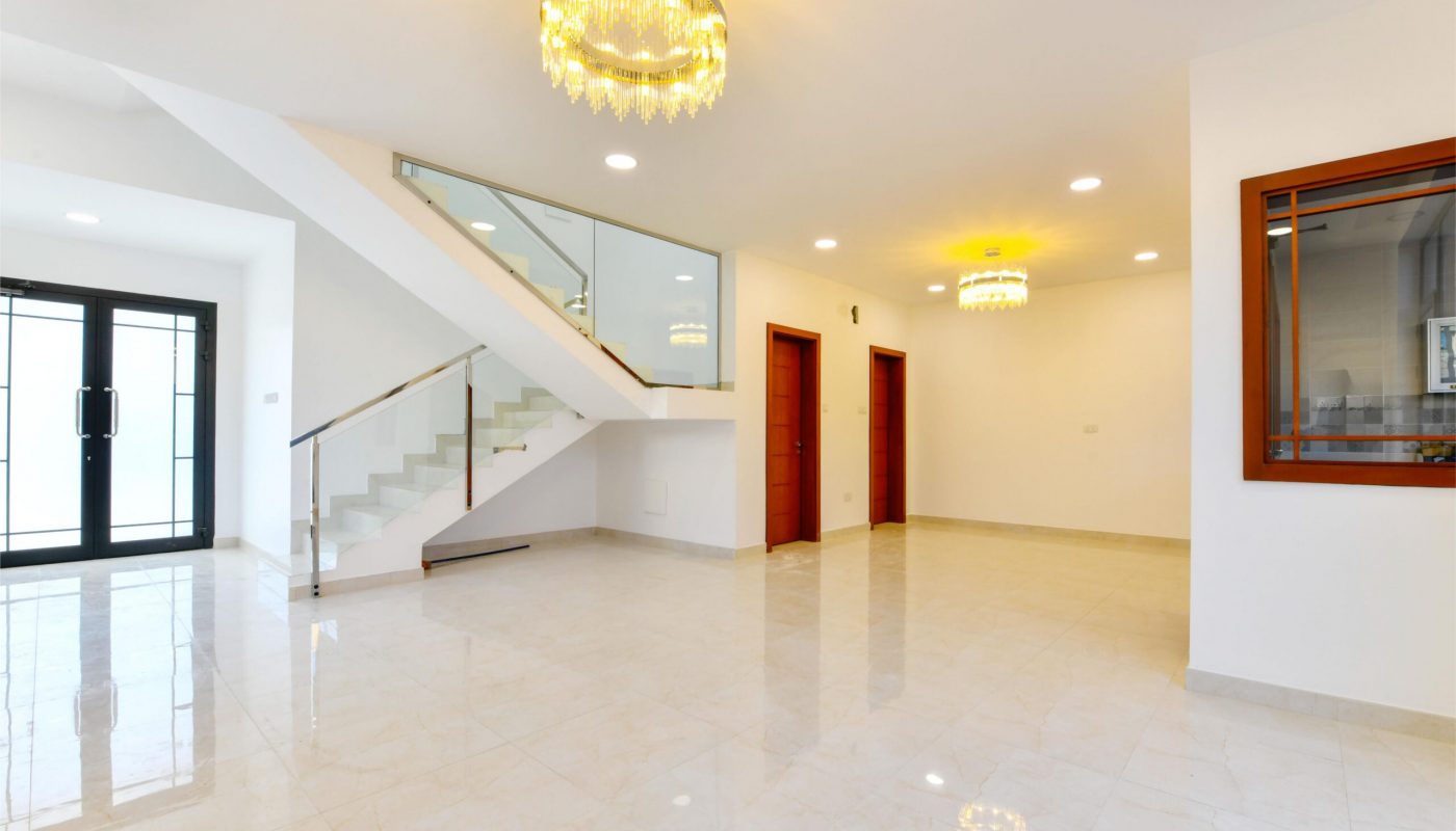 Spacious, modern living area with marble floors, glass stair railing, two chandeliers, red doors, and a large window looking into another room.