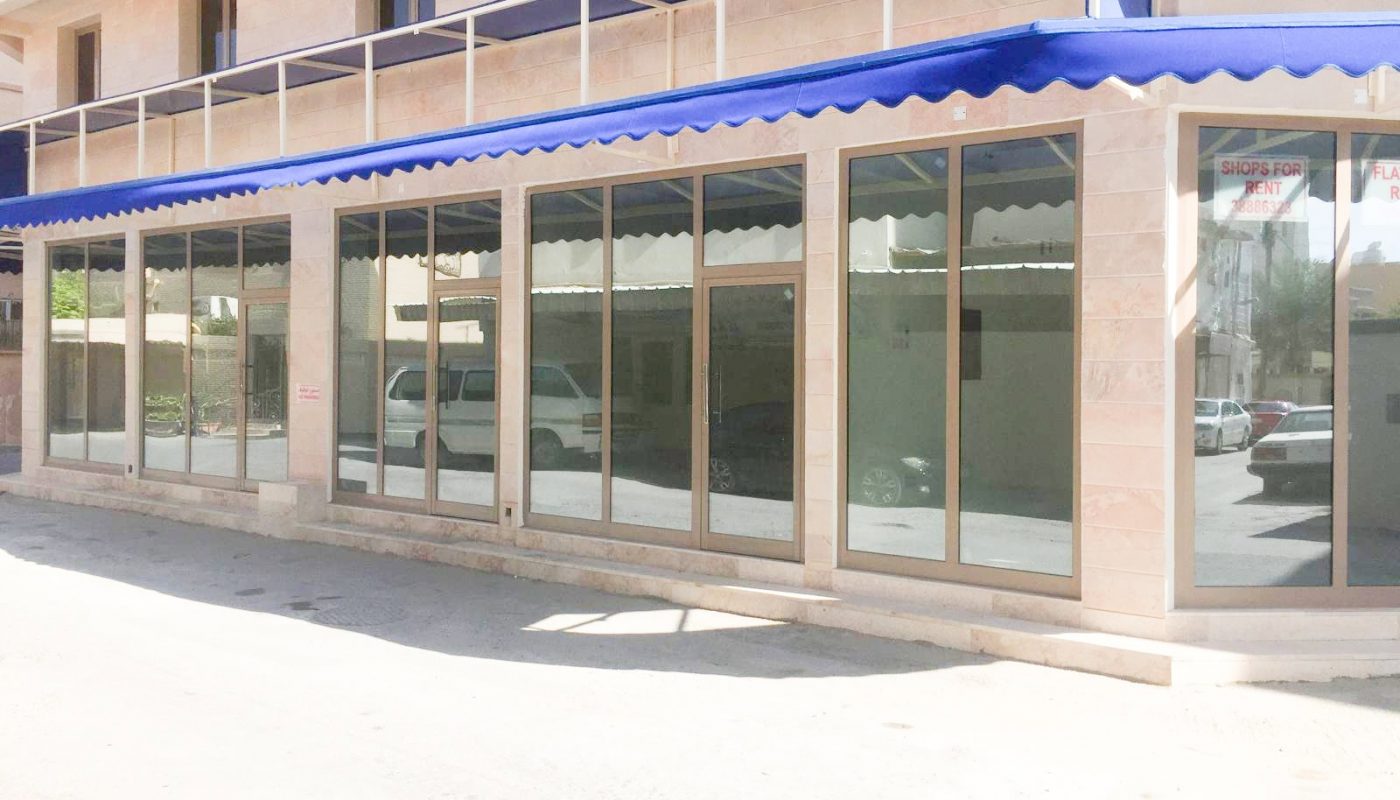 Street view of a building with large glass windows and a blue awning.