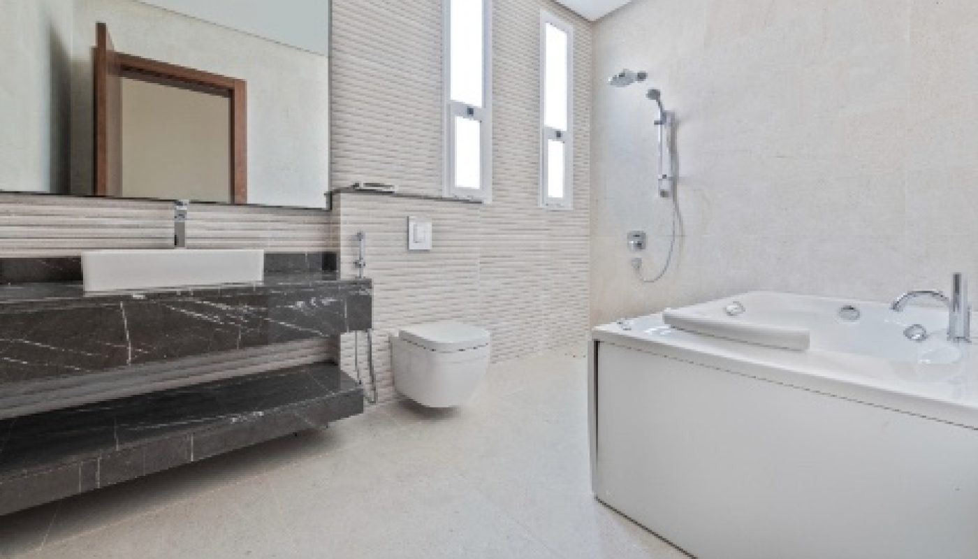 Modern bathroom with a large mirror, black countertop sink, wall-mounted toilet, and white bathtub, featuring light-colored tiles and two tall windows.
