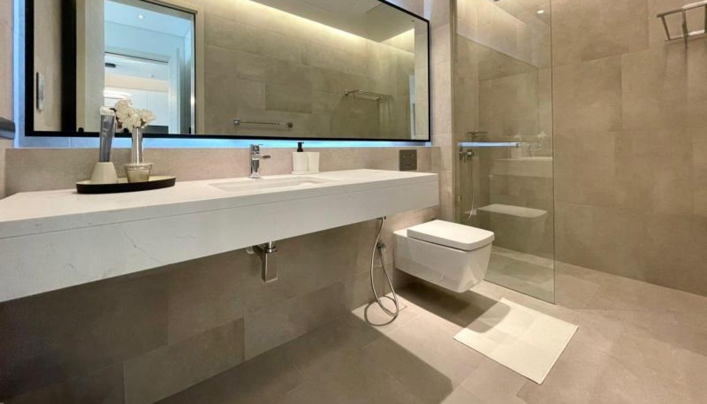 Modern bathroom with large mirror, floating sink, wall-mounted toilet, walk-in glass shower, and neutral-toned tiles. A white towel and decorative flowers are placed on the countertop.