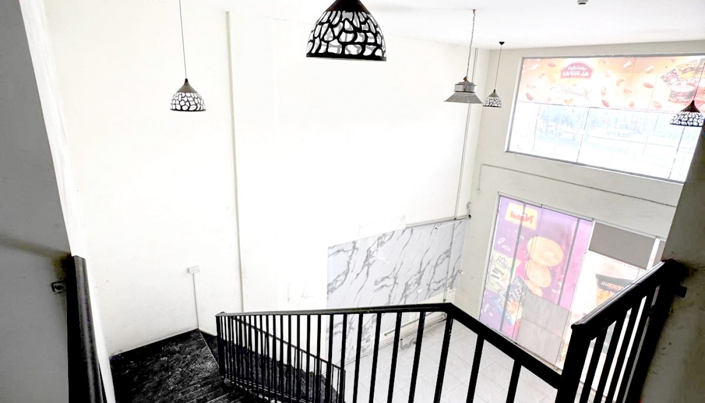 Black metal staircase with railing descending to a lower floor, white walls, three hanging pendant lights, and large windows letting in natural light.