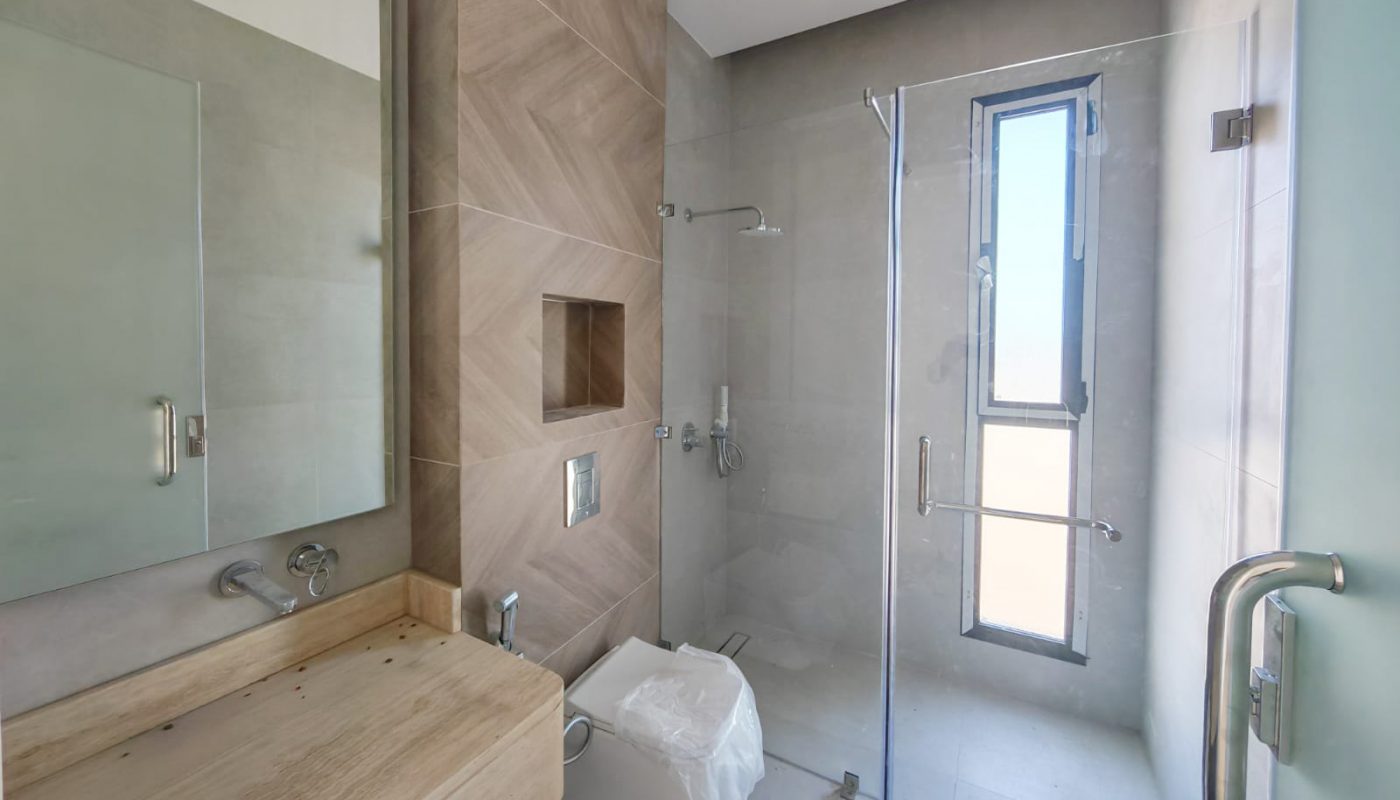 Modern bathroom with glass shower enclosure, wooden vanity, wall-mounted toilet, large mirrors, and natural light from a tall window.