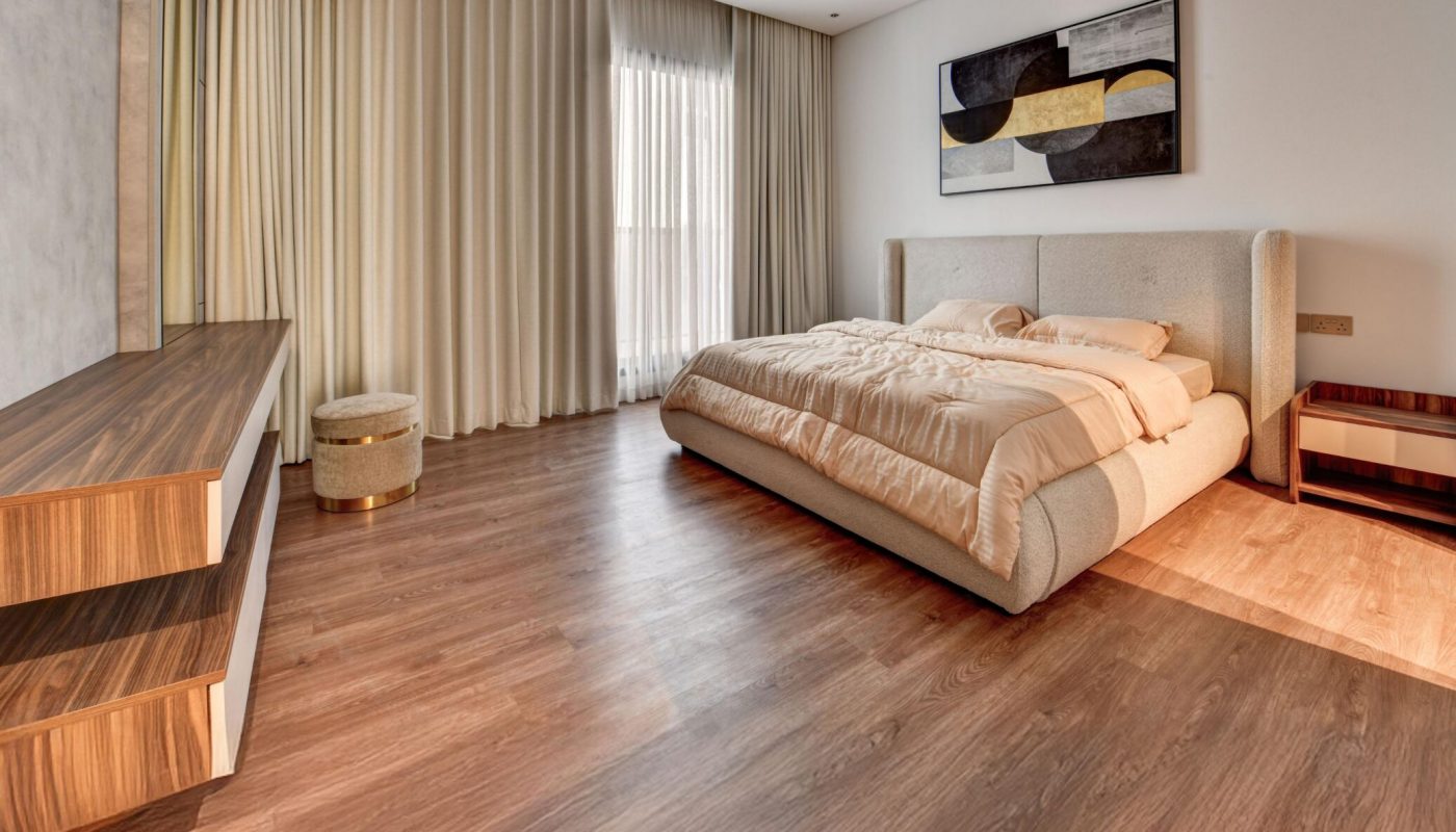 A modern bedroom with a large bed, wooden floors, low wooden furniture, floor-to-ceiling curtains, and abstract art on the wall.