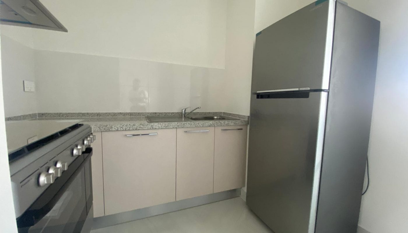 Modern kitchen with a stainless steel refrigerator, a stove, light-colored cabinets, granite countertops, and a sink in the corner.