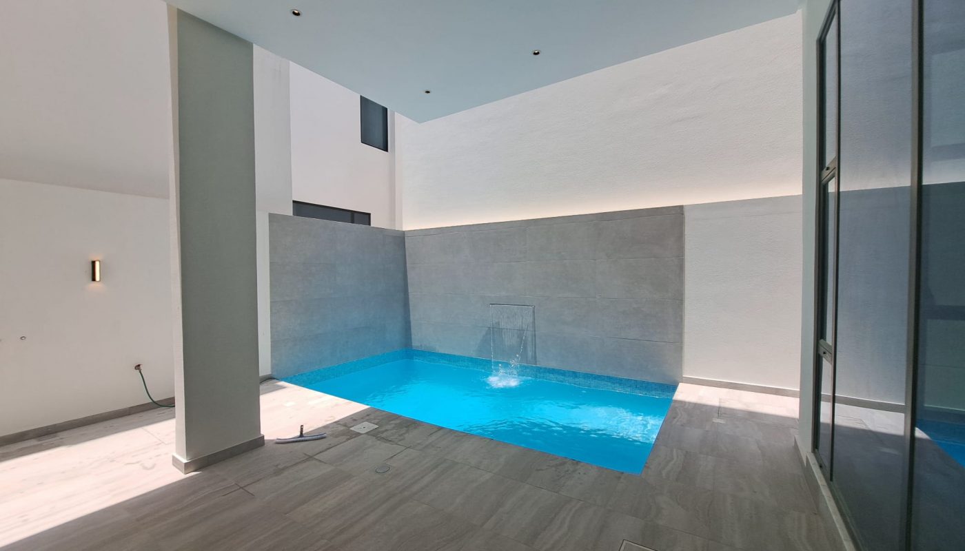 Indoor pool in a modern room with gray tiled floor and walls, glass doors on the right, and minimal lighting.