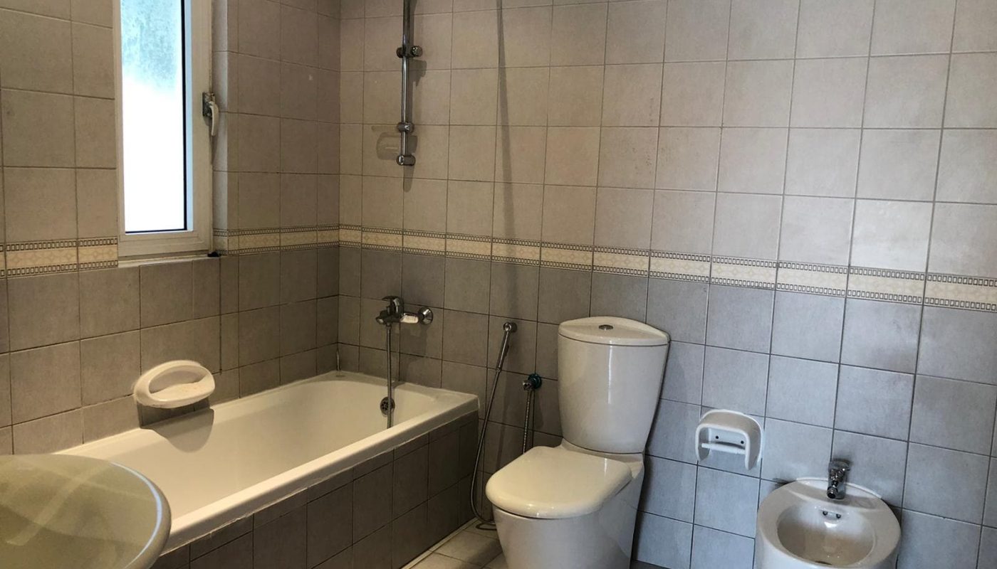 A modern bathroom in a semi-furnished 3 bedrooms villa, with a bathtub, toilet, bidet, sink, and a small window letting in natural light, tiled in neutral tones.