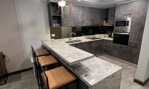 A luxury kitchen with marble counter tops and bar stools, fully furnished.