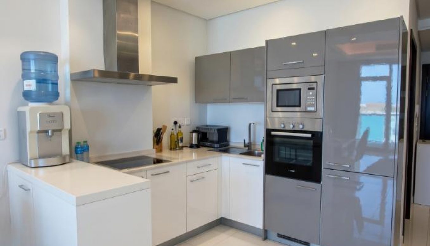 Modern kitchen with white cabinets, glossy gray appliances, a water dispenser, built-in oven, microwave, and induction cooktop, all set on a white tiled floor with recessed lighting.